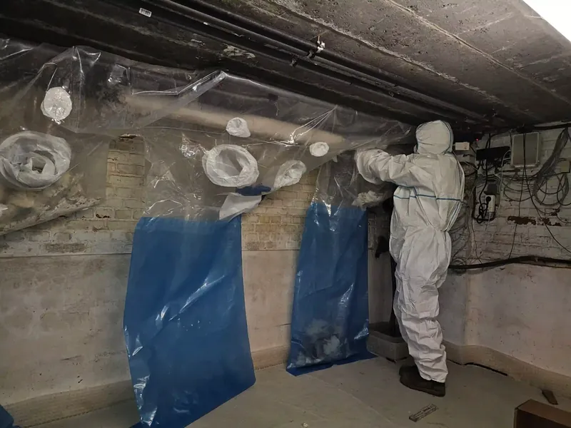 Un désamianteur travaille avec des sacs d'incubation sur des conduites dans une cave