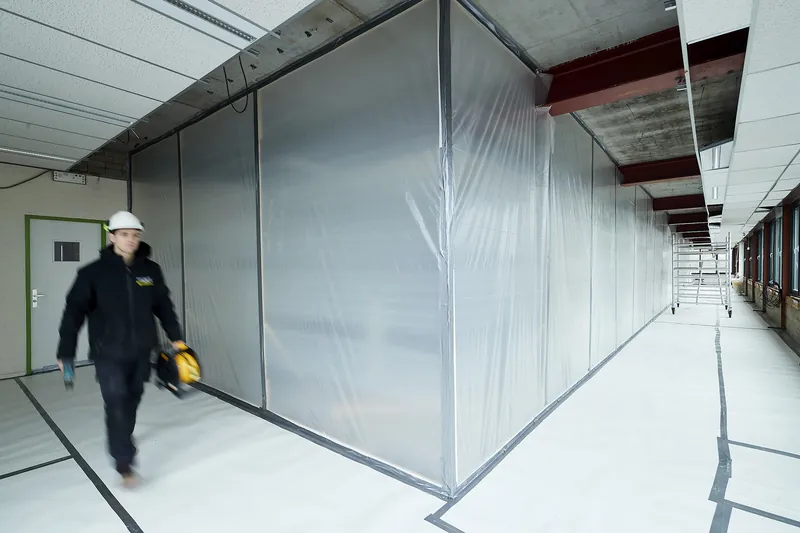 Un collaborateur longe une zone hermétique sous film plastique
