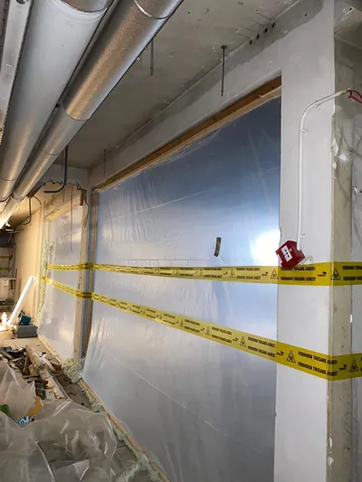 Couloir avec paroi en film plastique et ruban de signalisation autour d'une zone hermétique
